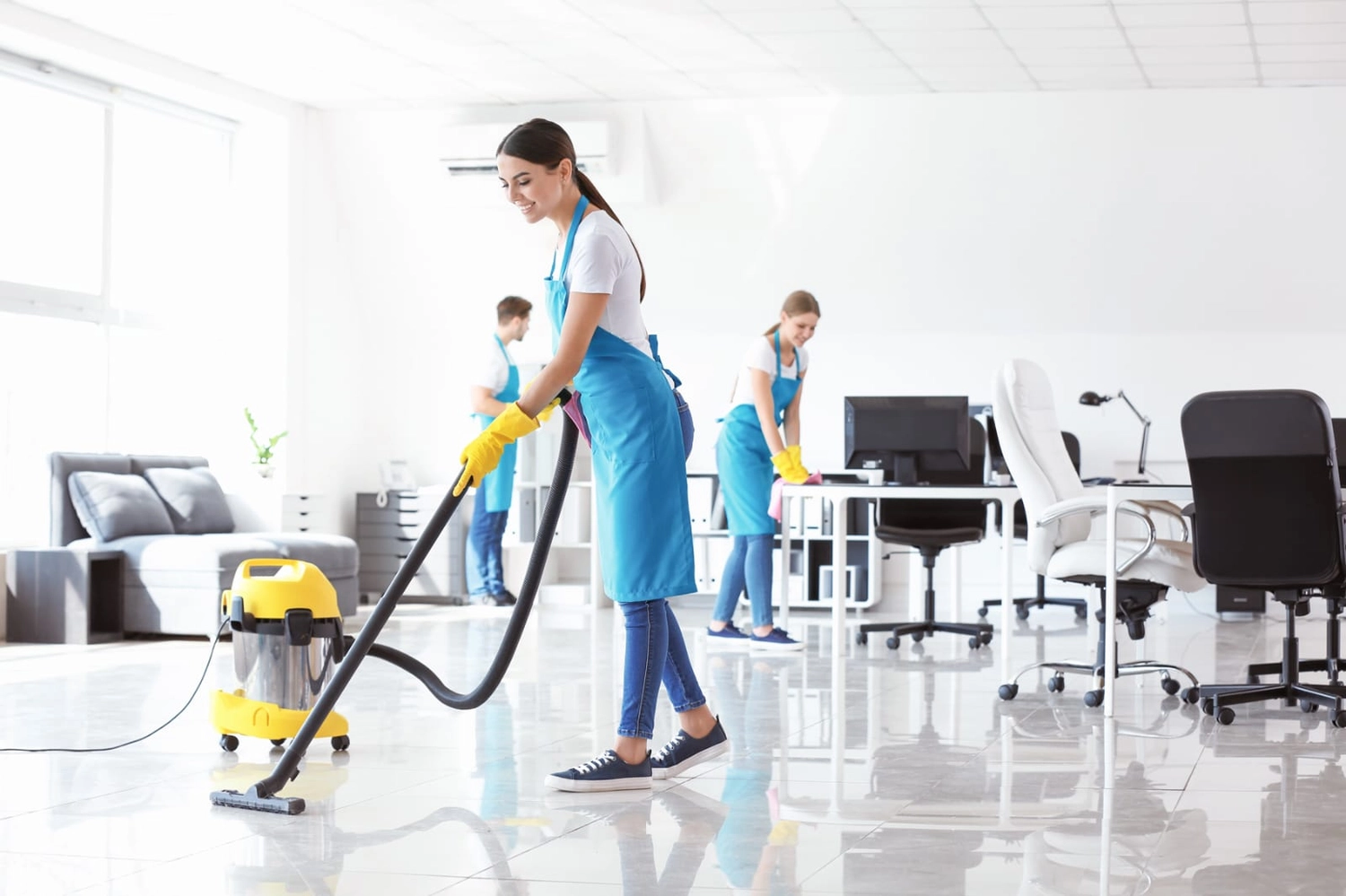 Simply Clean Niederrhein - Professionelle Reinigung - Professionelle Reinigungskräfte in blauen Schürzen und gelben Handschuhen säubern einen hellen, modernen Büroraum.